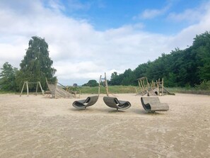 Une plage de sable avec trois balançoires en bois et un grand arbre en arrière-plan.
