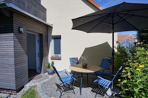 Un patio al aire libre con una mesa redonda, cuatro sillas azules, un paraguas negro grande y una planta en maceta.
