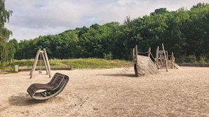 A sandy playground with a swing set and a wooden climbing structure.