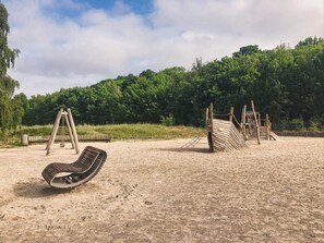 Une aire de jeux sablonneuse avec des balançoires et une structure d’escalade en bois.