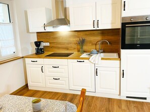 A kitchen with white cabinets, a wooden countertop, a coffee maker, a sink, and an oven. - Vacation apartment Irmchen - idyllic vacation in the Strelasund in Altefähr - (Altefähr)