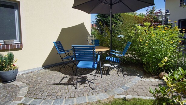 An outdoor patio with a table and chairs, a large umbrella, and potted plants.
