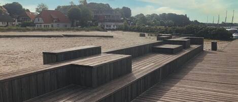 A wooden boardwalk leading to a sandy beach with steps and benches.
