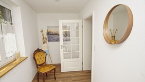 A hallway with a wooden chair, a white door, and a round mirror on the wall.
