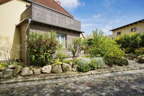 Une maison avec un chemin de pierre menant à l’entrée, entourée de différentes plantes et arbustes.