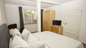 A bedroom with a bed, a TV on a stand, a wardrobe, and a window with curtains.