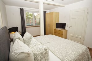 Une chambre à coucher avec un lit, un téléviseur posé sur un meuble, une armoire et une fenêtre avec des rideaux.