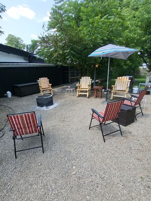 Et udendørs opholdsområde med Adirondack-stole, et bålsted og en stribet parasol.