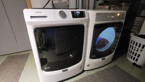Two white Maytag front-loading washers with digital displays, placed on a checkered floor with a laundry basket nearby. - Enjoyable 2 bedroom apartment with hot tub access.  (South Wales)
