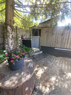 En træterrasse med en velkomstskilt, en potteplante og et lille udendørs område med trin op til en dør.