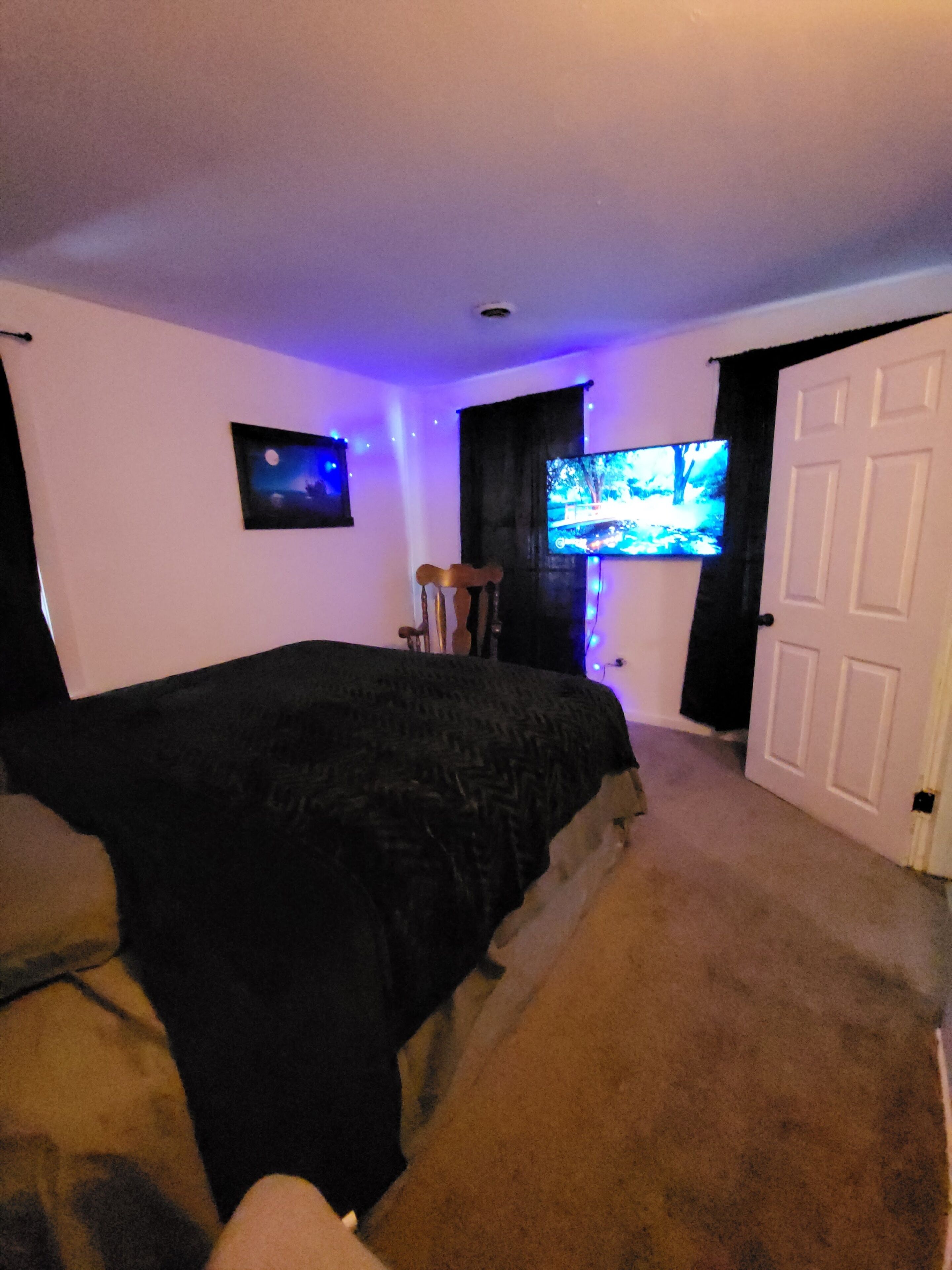 Une chambre à coucher avec un lit, un téléviseur, une porte et un tableau accroché au mur.