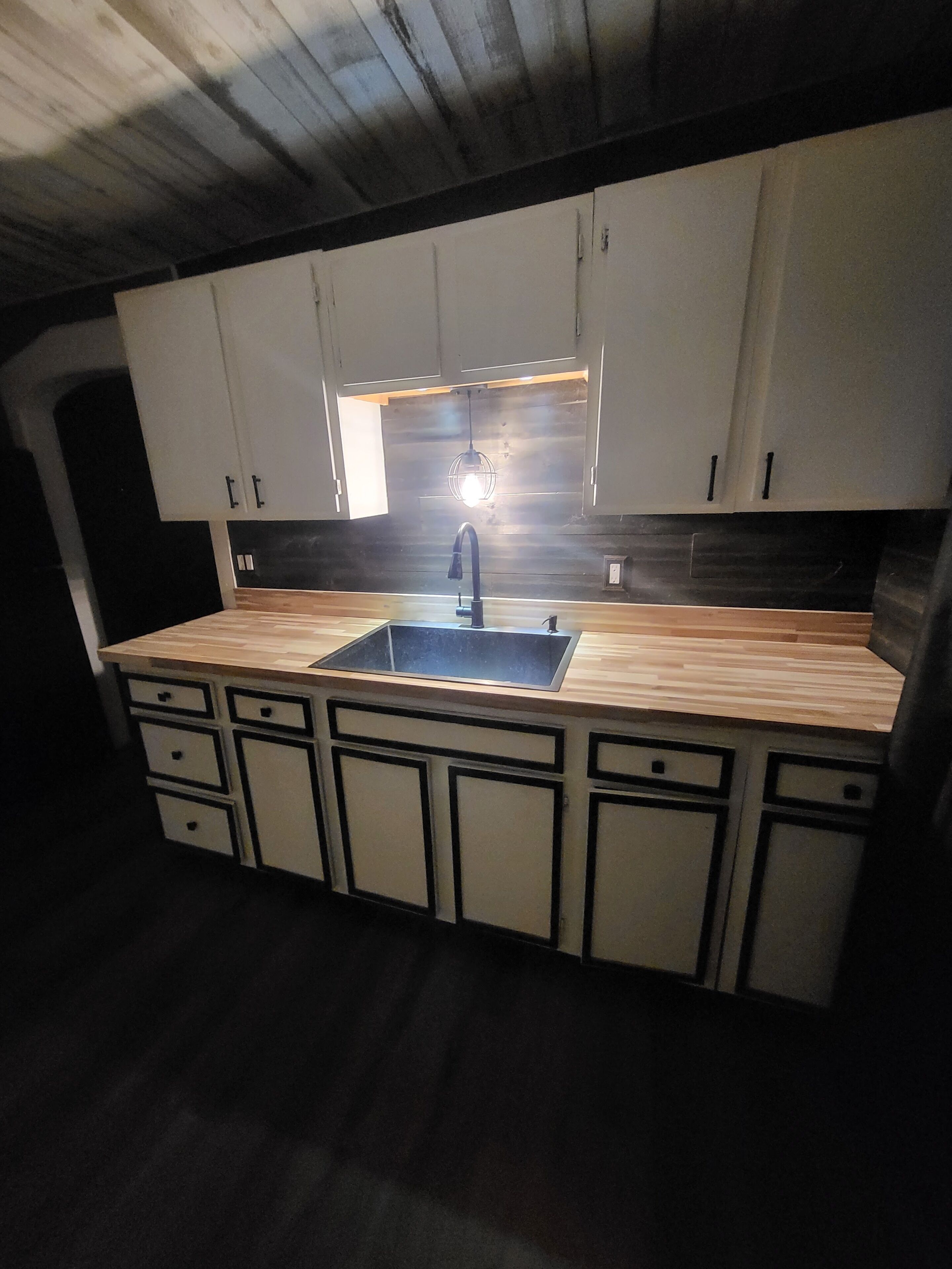 Uma cozinha com ilha central, armários brancos e bancada preta.