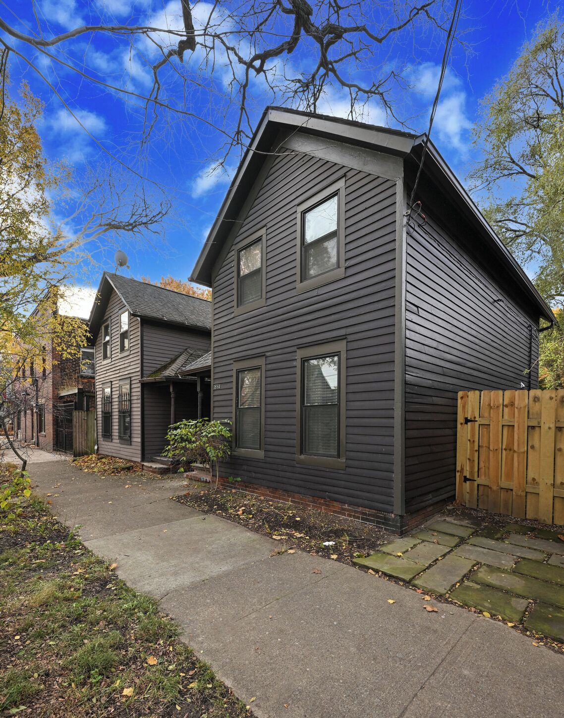A two-story residential house with a dark siding exterior, a visible front porch, and a wooden fence.
