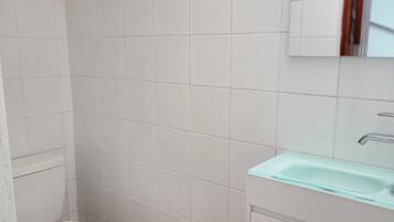 A small, clean bathroom with white tiles, a white toilet, and a light blue sink.