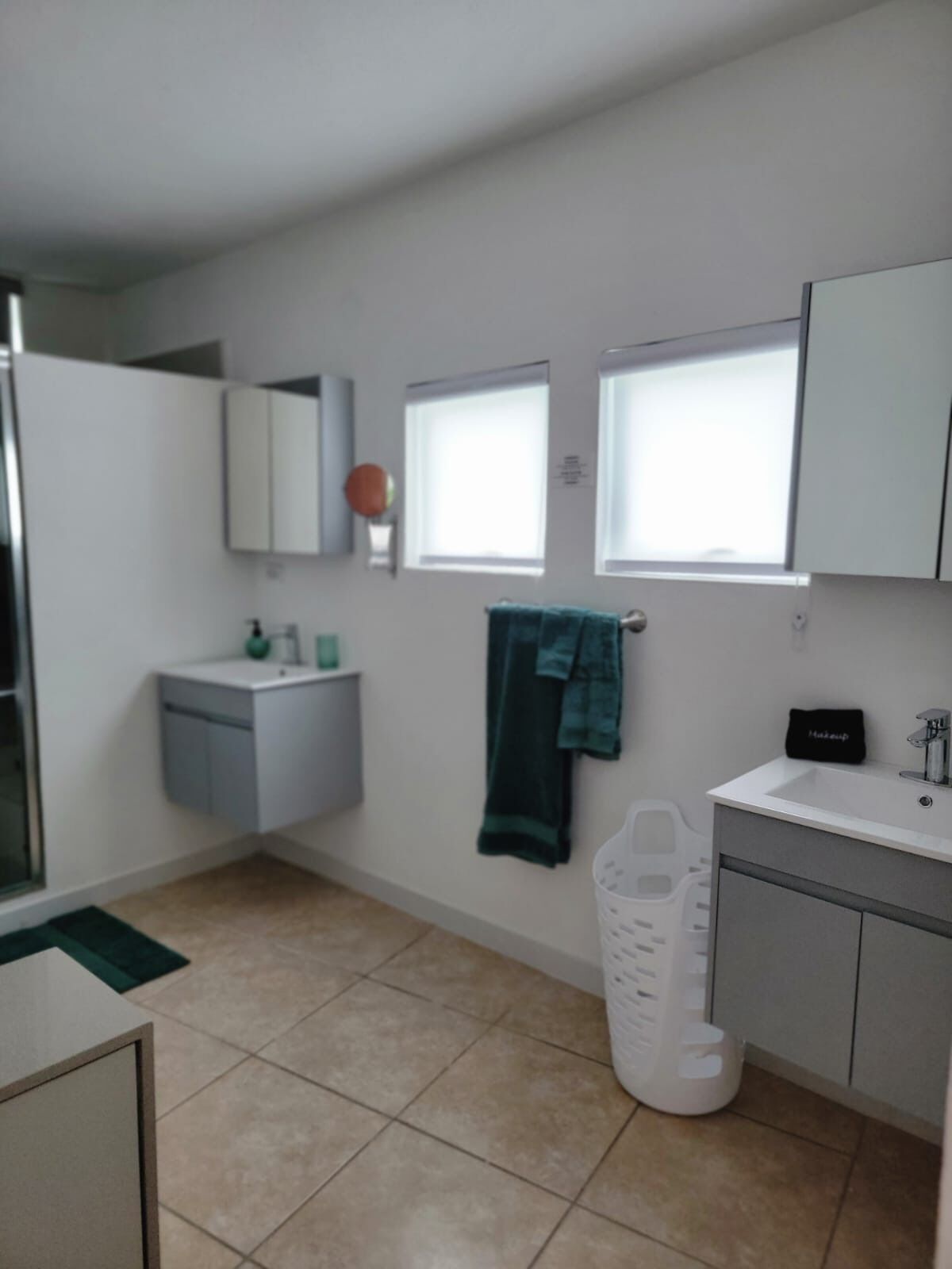 Een moderne badkamer met een witte wastafel, spiegel en kastjes. Er is een raam dat natuurlijk licht biedt en een handdoek hangt aan de muur.