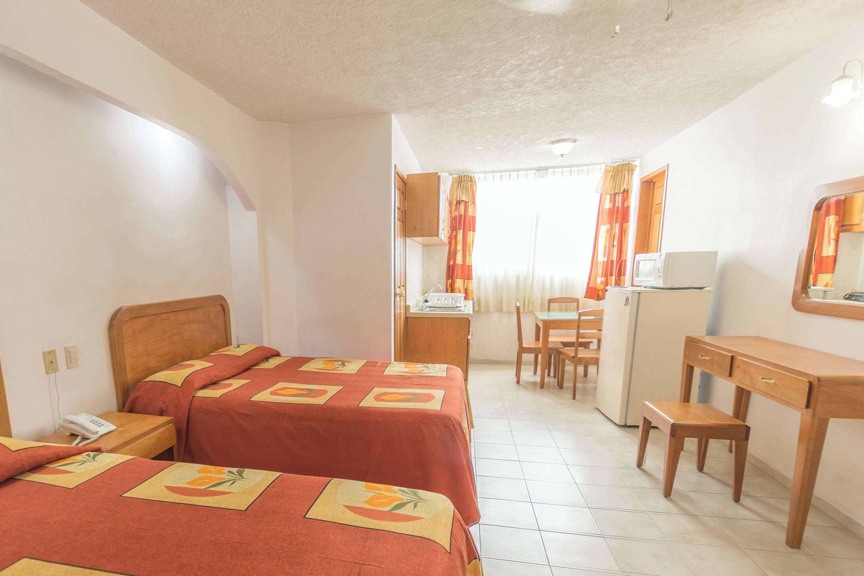 Quarto de hotel com duas camas, uma escrivaninha, uma cadeira, micro-ondas e frigorífico.