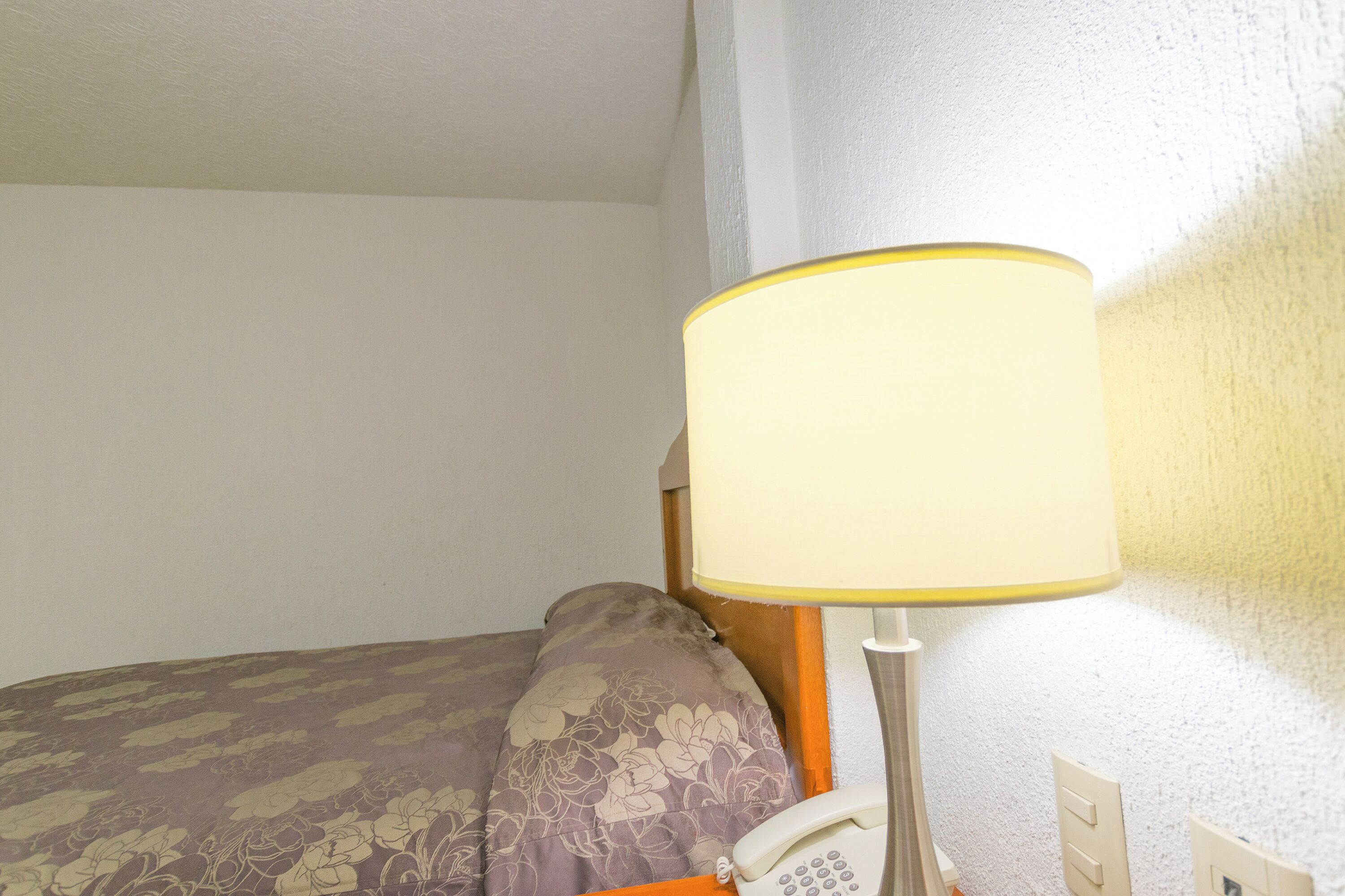 Una habitación de hotel con una cama, una lámpara de noche y un teléfono.