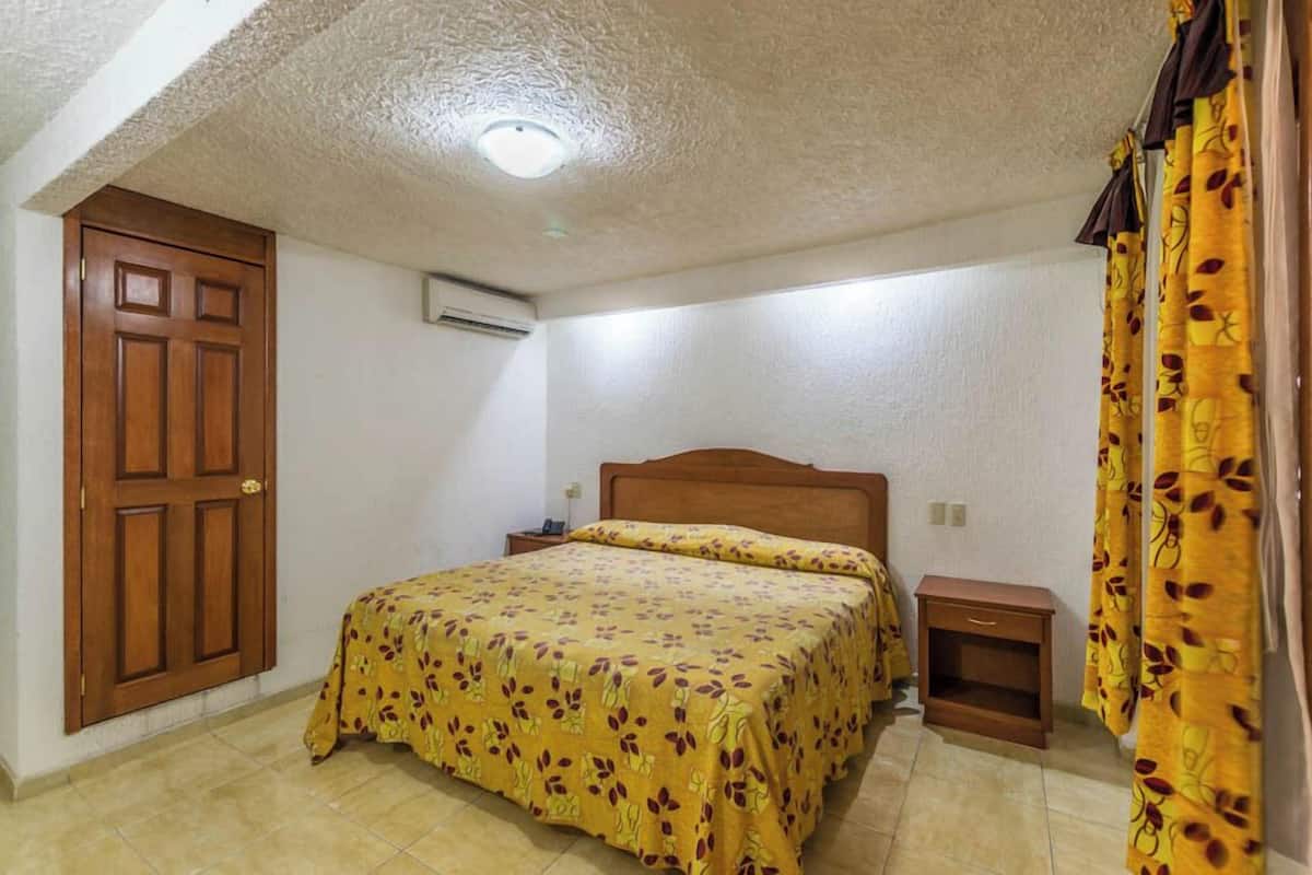 A bedroom with a wooden door, a bed with a floral bedspread, a nightstand, and a curtain.