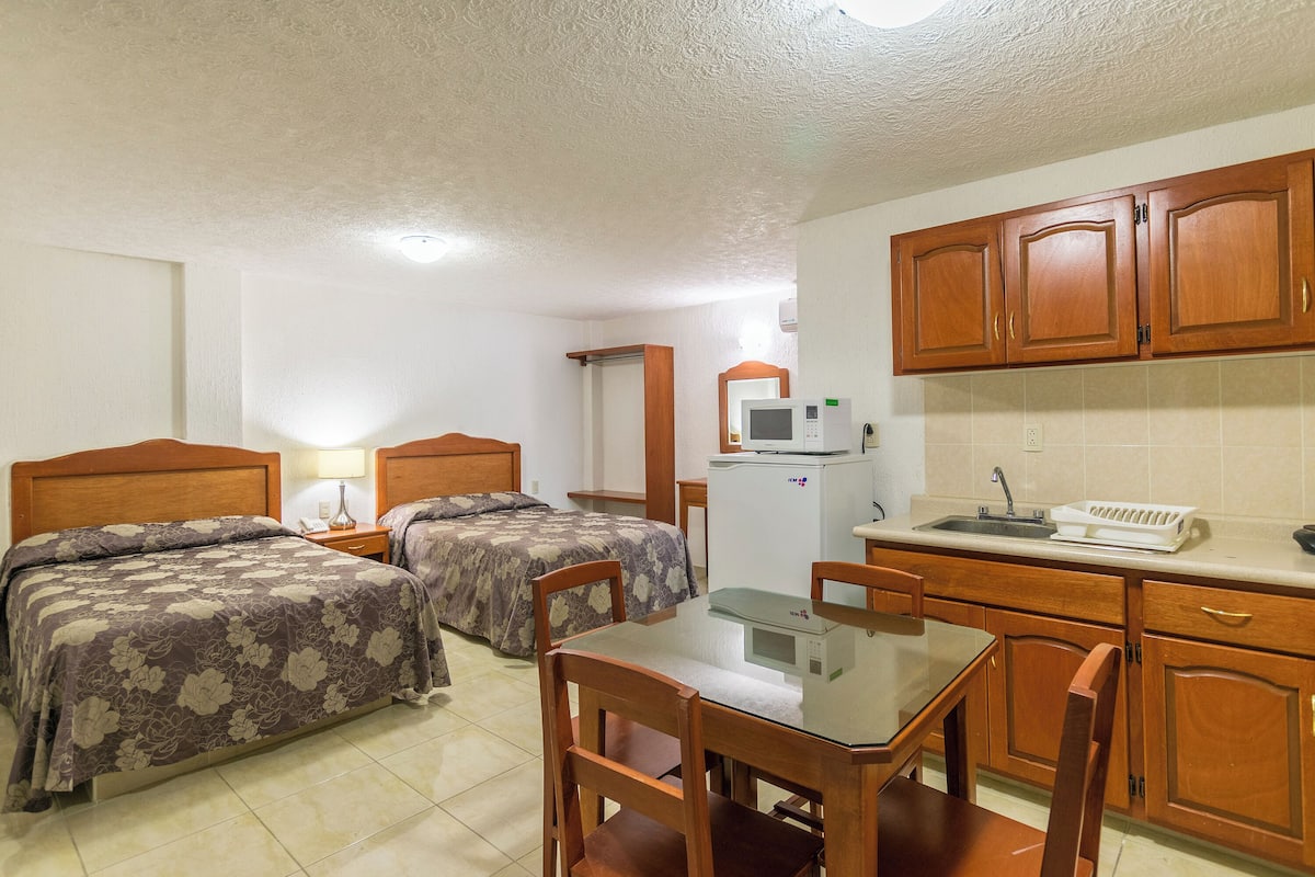A bedroom with two beds, a small kitchenette, and a dining area.