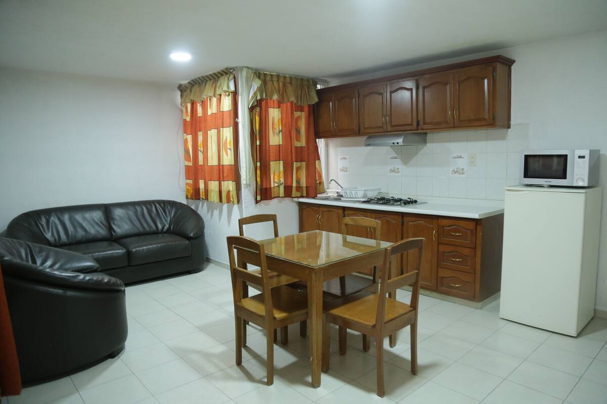 A compact kitchen with wooden cabinets, a white refrigerator, a microwave, and a dining table with chairs.