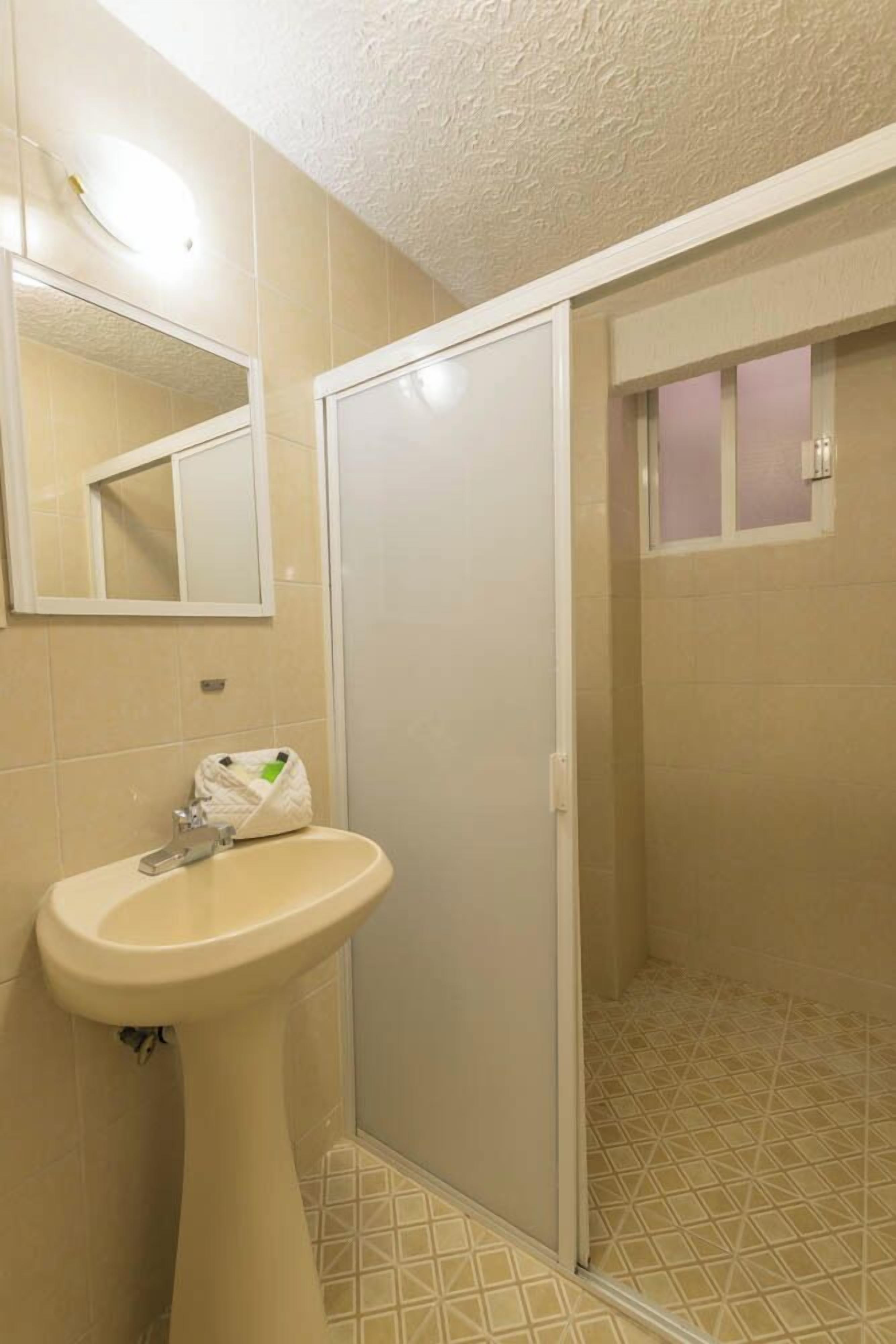 Un baño con lavamanos pedestal, espejo y zona de ducha.