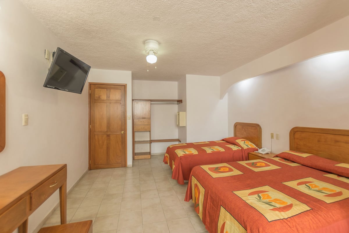 A hotel room with two beds, a desk, a TV mounted on the wall, and a ceiling fan.