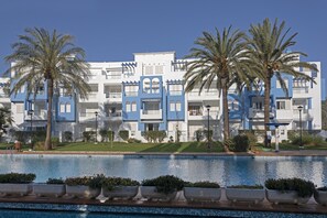 A modern hotel with a pool, palm trees, and a clear blue sky.