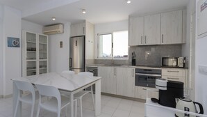 A modern kitchen with white cabinets, a dining table with chairs, and a coffee maker.