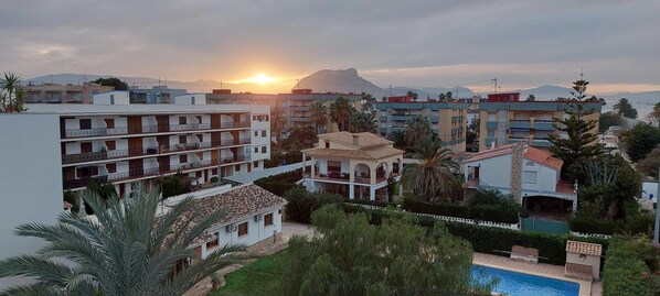A residential area with multiple buildings, a swimming pool, and a sunset in the background.