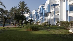 A row of modern white and blue buildings with balconies, surrounded by palm trees and a well-maintained lawn.