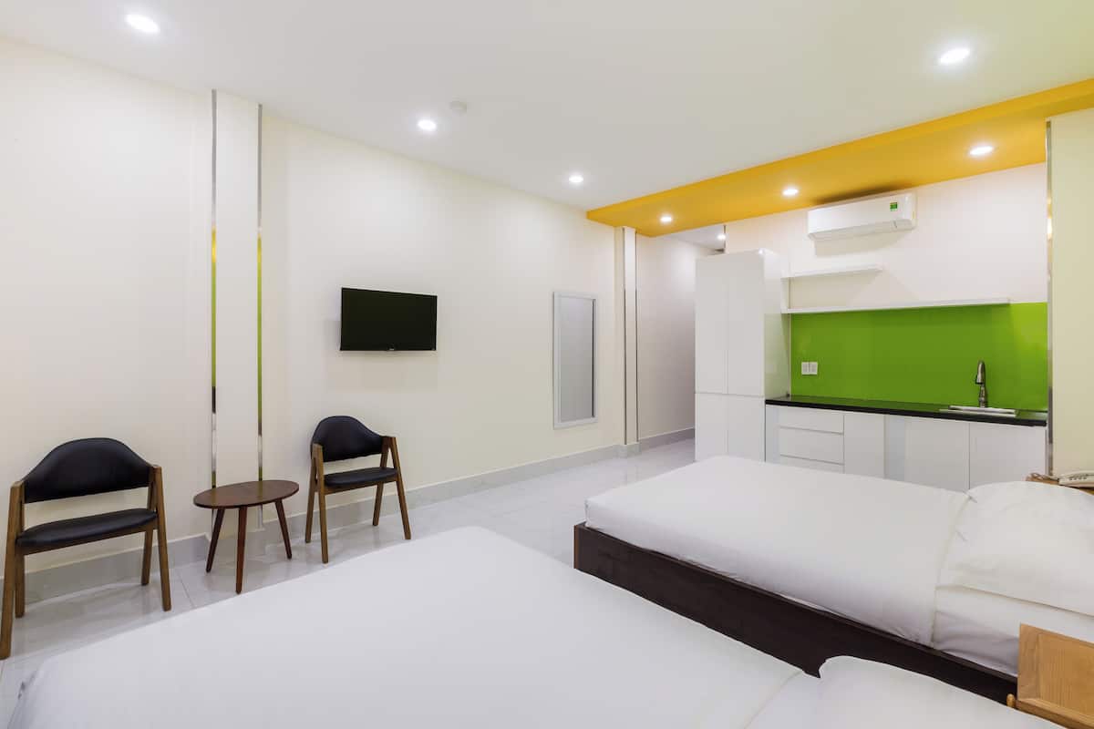 Quarto de hotel com duas camas, um pequeno espaço para refeições, televisão e cozinha compacta.