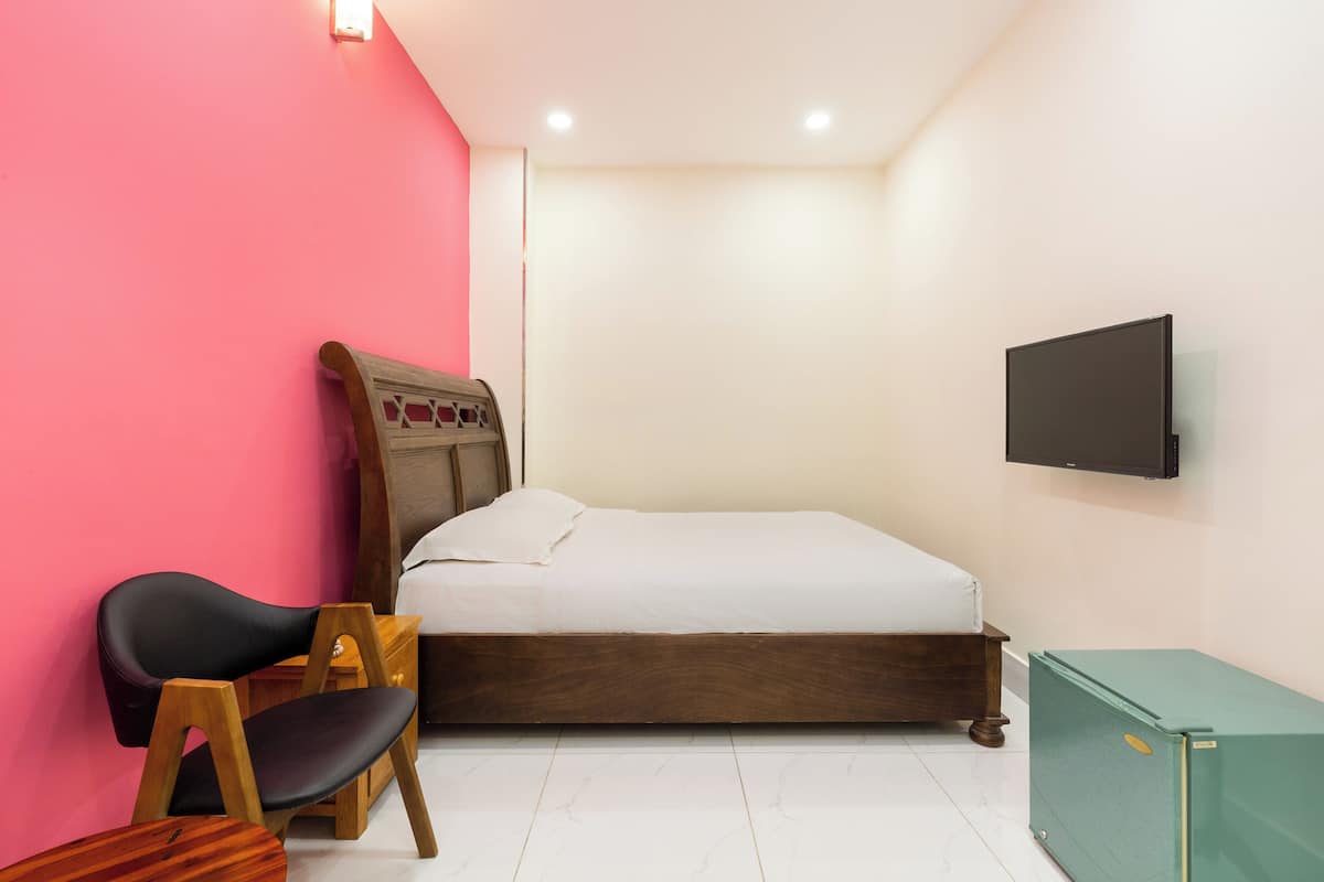 Quarto com uma cama, televisão fixada na parede, cadeira de madeira e um armário verde.