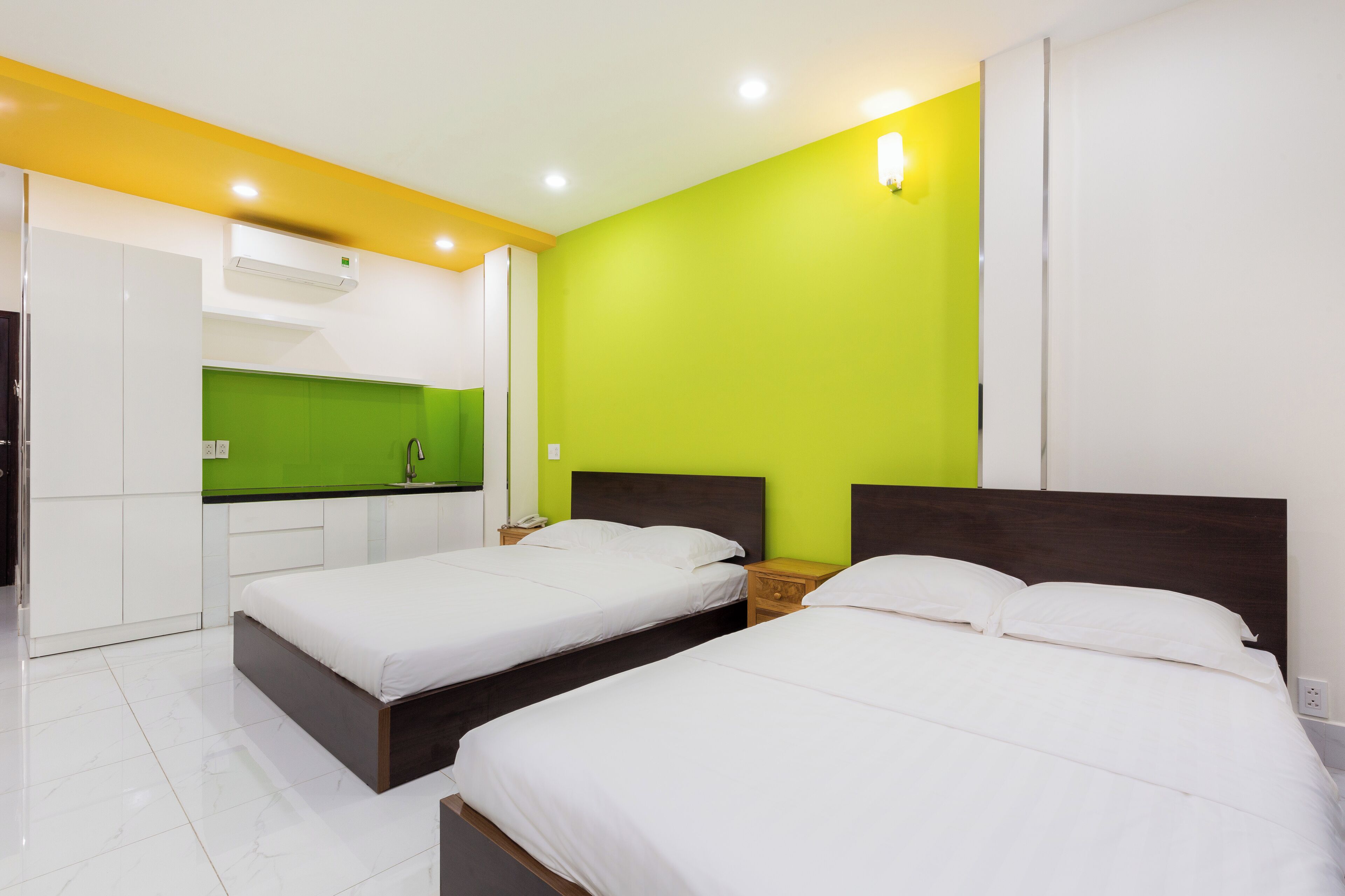 A hotel room with two beds, a kitchenette, and a green accent wall.
