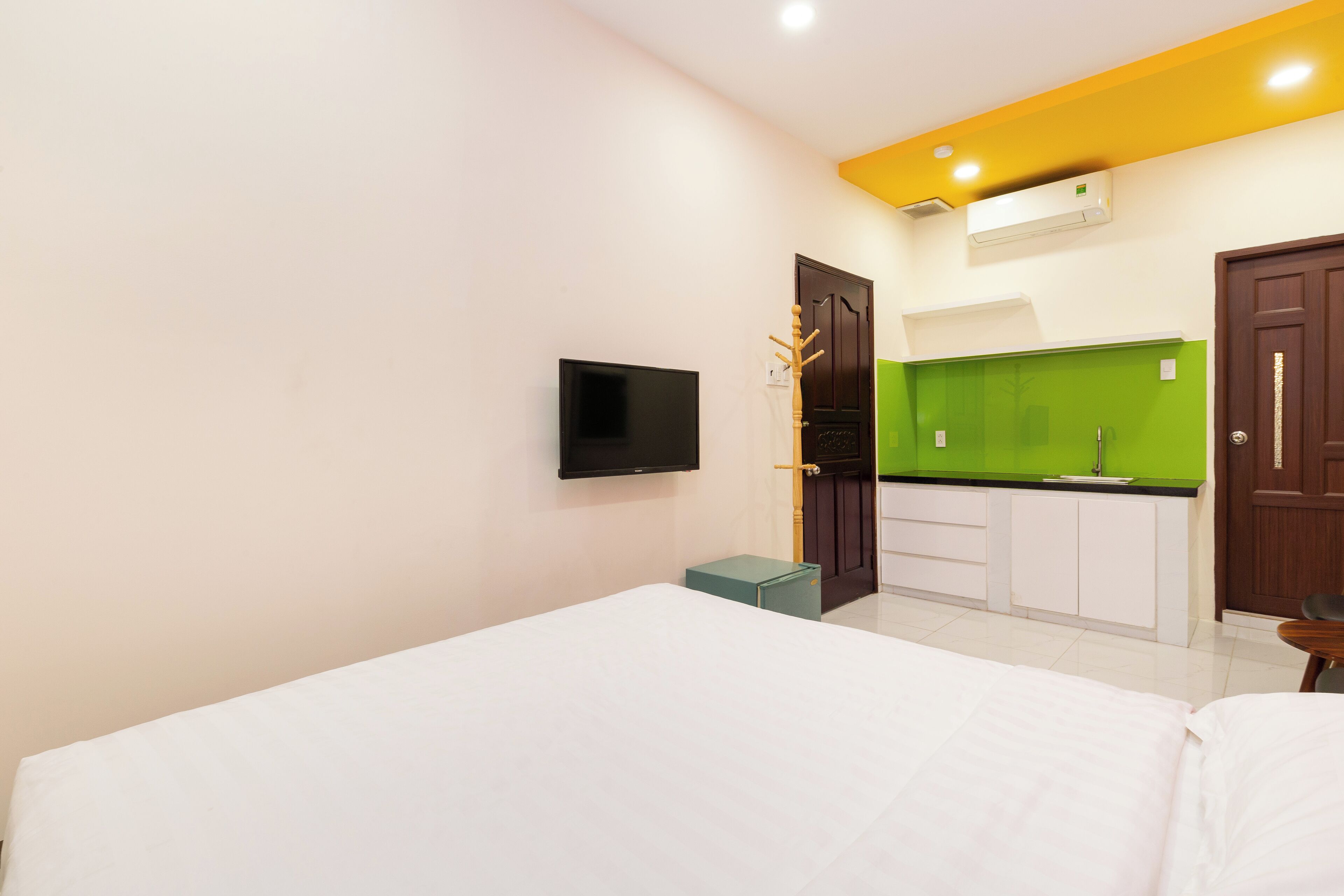 A hotel room with a bed, a TV, a kitchenette with green cabinets, and a door.