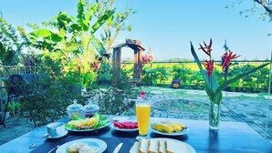 Un tavolo da pranzo all'aperto con prodotti per la colazione, tra cui uova, pane tostato, banane e un bicchiere di succo d'arancia.