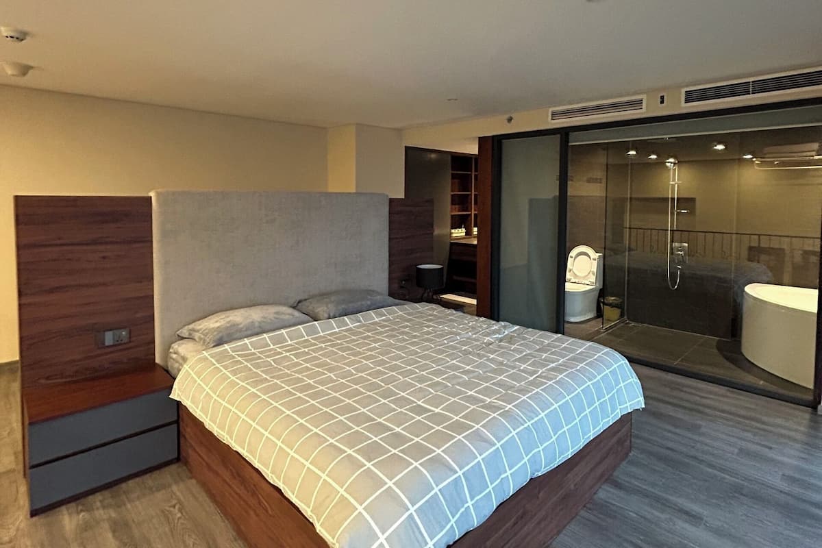 A modern bedroom with a wooden bed, a built-in bench, and a glass shower enclosure.