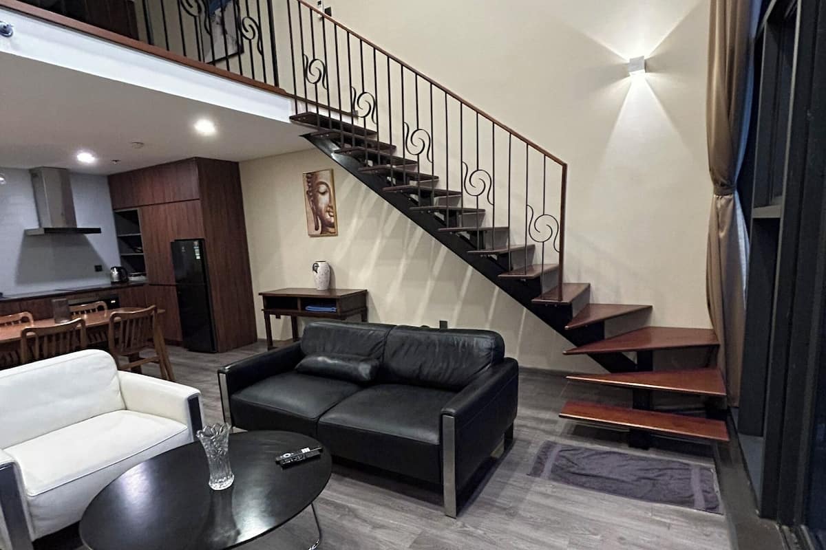 A spacious living area with a black leather sofa, a small round table, and a staircase with a metal railing.