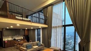 Un'ampia zona giorno con divano, tavolino e tavolo da pranzo. Si intravede un balcone con ringhiera e, attraverso ampie finestre, si può ammirare una vista sulla città.