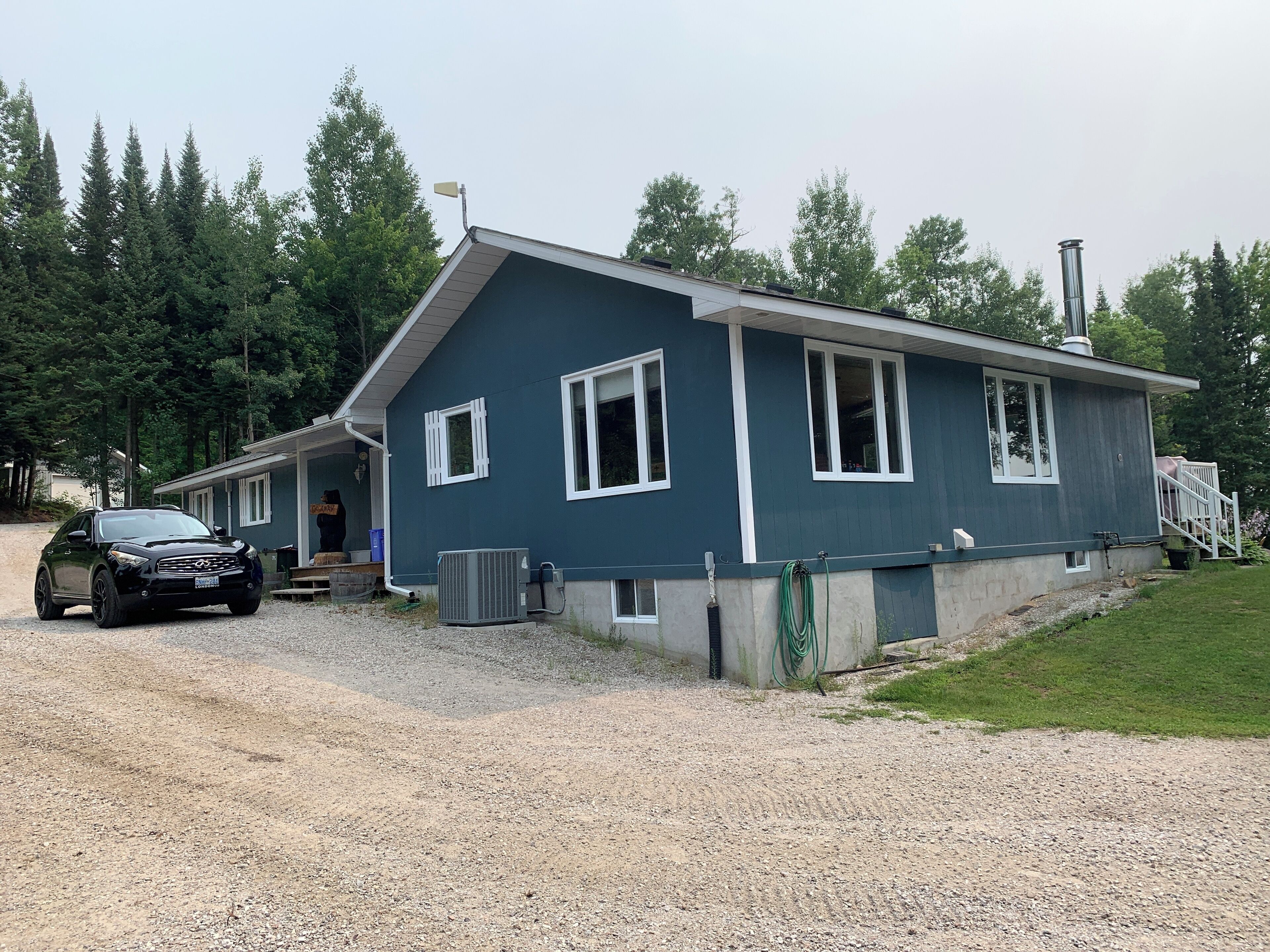 A two-story house with a gravel driveway, a parked car, and a green lawn.