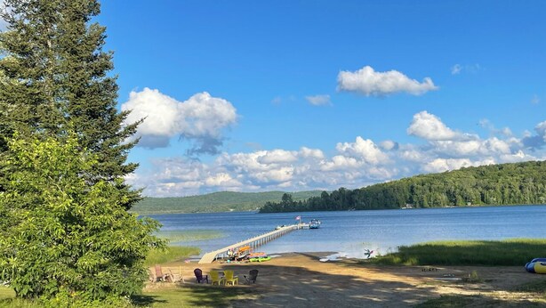 A lakeside view with a dock extending into the water, surrounded by greenery and a clear sky. - Family-Friendly Cottage with all the Amenities You Need!  (Burk's Falls)