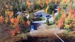 An aerial view of a property with multiple buildings, surrounded by dense forest with autumn foliage. - Family-Friendly Cottage with all the Amenities You Need!  (Burk's Falls)
