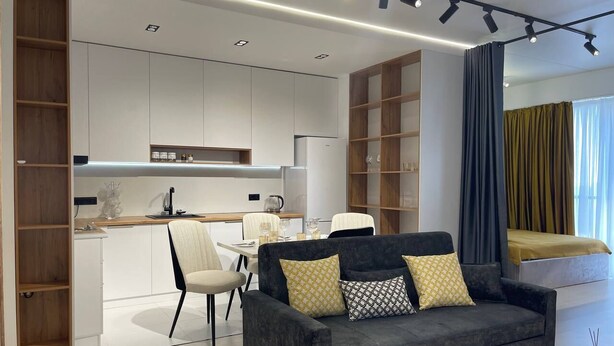 A modern living room with a dark grey sofa, a white coffee table, and a dining area with a white table and chairs. - Akay city Golden studio (Tashkent)