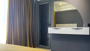 A modern hotel room with a bed, a built-in desk, a mirror, and a window with blinds. - Akay city Golden studio (Tashkent)
