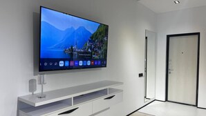 A modern living room with a flat-screen TV mounted on a white wall, a minimalist entertainment unit below, and a door to the right. - Akay city Golden studio (Tashkent)