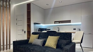 A modern living room with a dark grey sofa, two patterned cushions, and a small white table with a decorative item. - Akay city Golden studio (Tashkent)