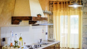 A kitchen with a stone wall, wooden cabinets, a tiled backsplash, and a window with curtains. - Charming Holiday Home With Garden (Tar-Vabriga)