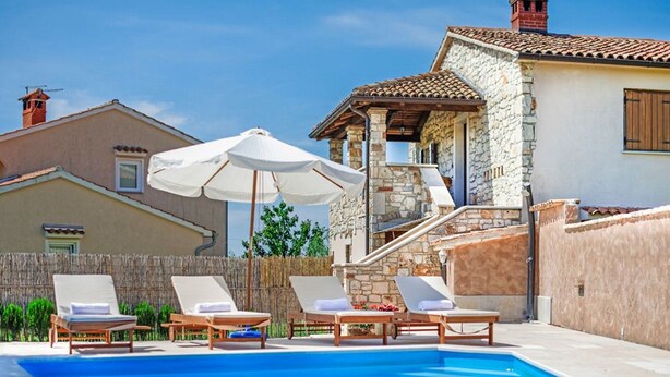 A swimming pool with lounge chairs and umbrellas, surrounded by stone and stucco buildings. - Charming Holiday Home With Garden (Tar-Vabriga)