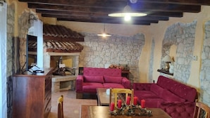 A rustic living room with stone walls, a wooden ceiling, a fireplace, a red sofa, a dining table with candles, and a wooden cabinet. - Charming Holiday Home With Garden (Tar-Vabriga)