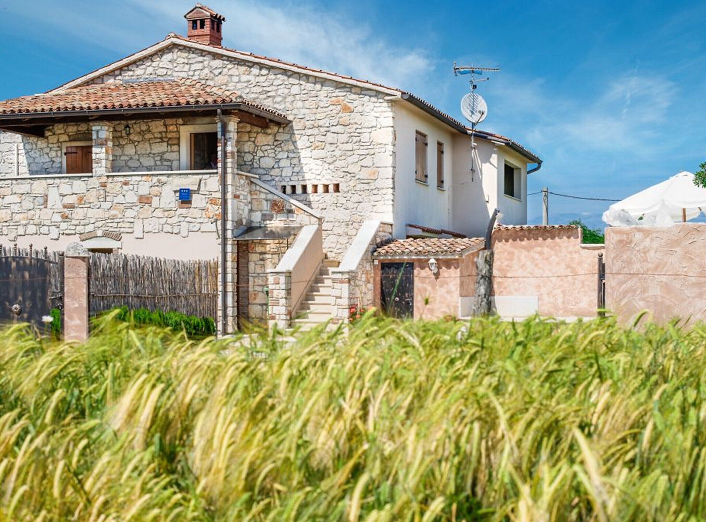 A stone house with a tiled roof, a staircase leading to the entrance, and a small garden area.