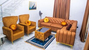 A living room with a sofa, two armchairs, a coffee table, and a fan. A staircase is visible in the background. - 4-Bedroom Duplex with Private Bathrooms in all Rooms (Lekki-Ajah Express Way)